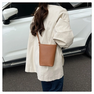 Modell im Freien mit brauner Eimer-Tasche aus Lychee-Leder und geprägtem Logo