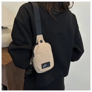 Rear view of a model wearing a minimalist beige nylon chest bag with black straps