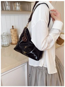 Detail of a black glossy leather tote bag with gold lettering and cookie pendant charm