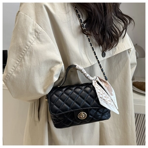 Close-up of black quilted leather handbag with gold twist lock and silk scarf handle
