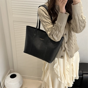 Minimalistische schwarze Leder-Tote-Bag mit Goldbeschriftung, getragen von einem Model