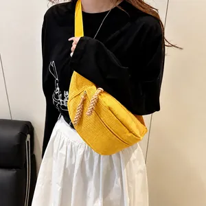 Detail of yellow corduroy crossbody bag with woven zipper pull on a female model