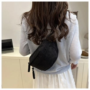 Detail of black corduroy crossbody bag with woven zipper pull on a female model