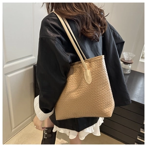 Detail of woven texture on camel leather tote bag carried by a model in black coat