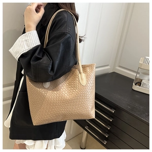 Close-up of beige woven tote bag with leather straps worn by model in a minimalist setting
