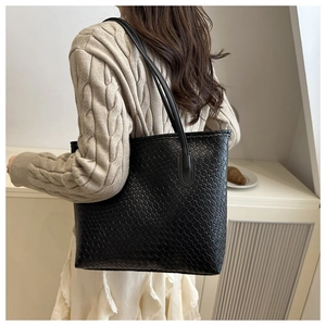 Detail of the black woven tote bag with textured diagonal pattern on female model shoulder