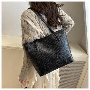 Detail of black woven tote bag with intricate checkerboard pattern and slim shoulder straps
