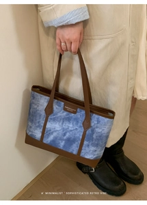 Detail of blue tie-dye tote bag with brown leather handles held by a model