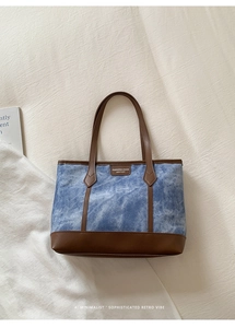 Detailed macro view of the blue denim canvas texture and brown leather stitching on tote bag