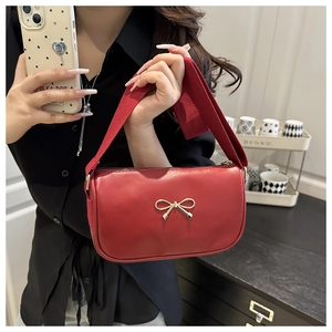 Detail of red leather bag with golden bow and wide shoulder strap held by model