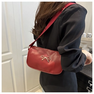 Detail of red leather shoulder bag featuring a decorative golden metal bow on the front