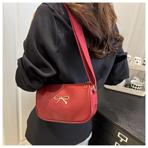 Detail of red leather crossbody bag with golden bow and canvas strap on shoulder