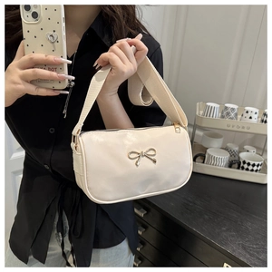 Detail of cream shoulder bag with golden bow clasp and wide canvas strap on model