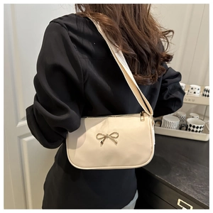 Close-up of off-white shoulder bag featuring a golden bow and wide strap on a model