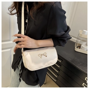 Detail of a beige crossbody bag featuring a golden bow metal buckle and wide textile strap
