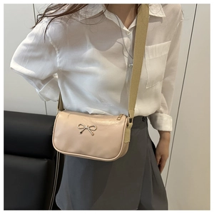 Close-up of beige crossbody bag with golden bow and wide canvas shoulder strap