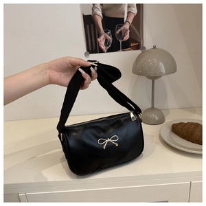 Detail of elegant black shoulder bag featuring gold metal bow buckle and wide fabric strap