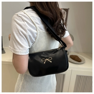 Detail of a black leather underarm bag with a gold bow buckle on a model shoulder
