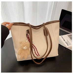 Detail of large beige tote bag with brown trim and cute teddy bear pendant on table