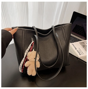 Detail of black pebbled leather tote with plush bear charm in office setting