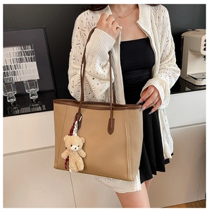 Detail of khaki lychee grain tote bag with plush bear charm and brown leather handles