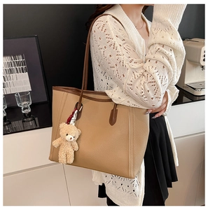 Close-up of khaki tote bag with lychee grain texture and cute plush bear pendant accessory