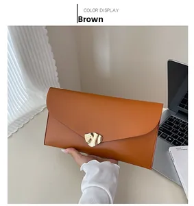 Détail d'une pochette enveloppe en cuir mat marron avec un fermoir magnétique doré