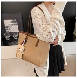 Detail of camel pebbled leather tote bag with a cute brown plush bear charm pendant