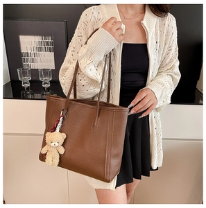 Close-up of brown pebbled leather tote bag featuring a cute plush bear charm detail