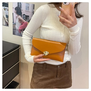 Détail d'une pochette enveloppe en cuir marron avec une boucle en métal doré en forme de feuille