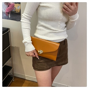 Détail d'une pochette enveloppe en cuir jaune moutarde avec boucle dorée aimantée