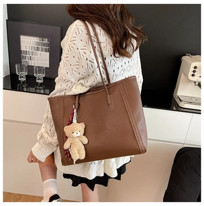 Close-up of brown litchi textured tote bag with cute plush bear charm and ribbon