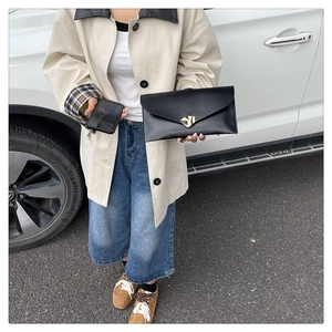 Detail of a black envelope clutch featuring a gold heart-shaped metal buckle on matte leather