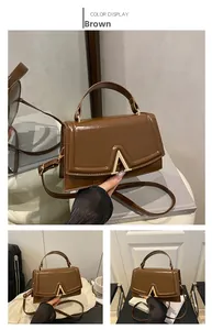 Detail of a brown patent leather crossbody bag featuring a golden V-shaped buckle hardware