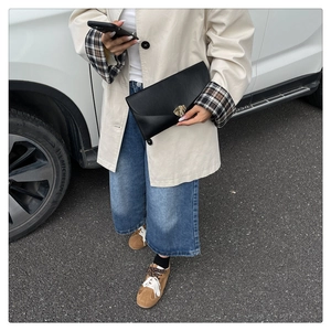 Detail view of a black leather envelope clutch featuring a gold leaf-shaped metal buckle