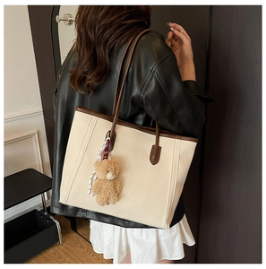 Detail of a large cream tote bag with brown straps and a plush bear charm on a model