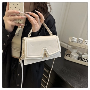 Detail of a chic cream leather handbag featuring a signature gold V-shaped metal clasp