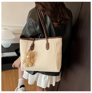 Detail view of a beige leather tote bag with brown trim and plush bear pendant detail