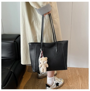 Detail of black lychee grain leather tote bag with a cute beige plush bear pendant