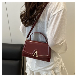 Close-up of burgundy leather crossbody bag with distinctive gold V-shaped metal buckle