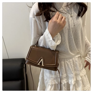 Detail of a brown leather crossbody bag with a distinctive V-shaped gold metal buckle