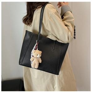 Detail of black pebbled leather tote bag featuring a cute plush bear and silk scarf charm
