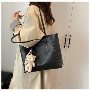 Detailed view of large black litchi pattern tote bag with bear charm on model shoulder