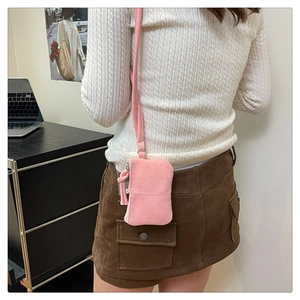 Close-up of pink faux suede mini lipstick bag with crossbody strap on a white sweater