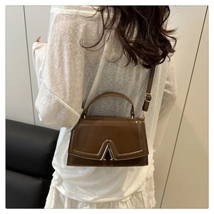 Detail of a brown leather crossbody bag with a metal V-shaped clasp on a model