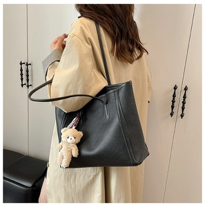 Detail of a large black tote bag with litchi texture and a cute brown bear charm