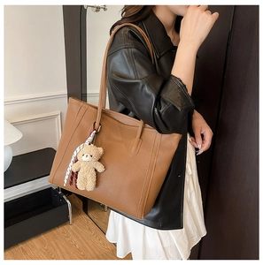 Detail of brown lychee leather tote bag featuring a cute bear charm and plaid silk scarf