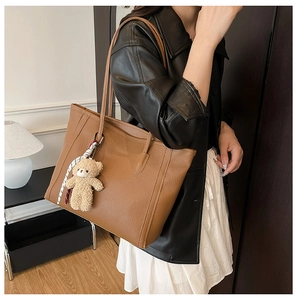 Detail of a brown lychee pattern leather tote bag with a cute bear plush pendant charm