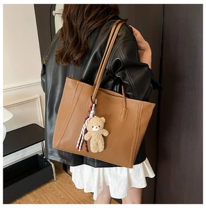Detail of brown tote bag featuring litchi grain texture and cute plush bear charm