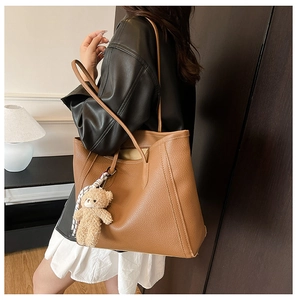Brown tote bag with bear charm and scarf detail shown on shoulder of model in leather jacket